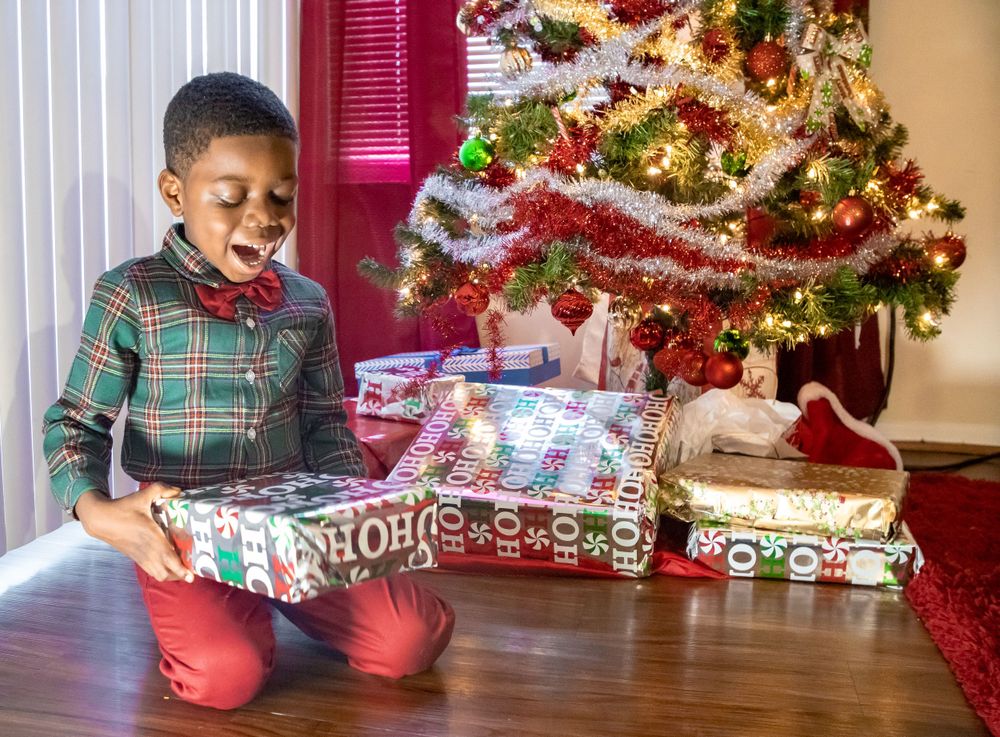 Child sitting with wrapped Christmas presents near decorated tree.