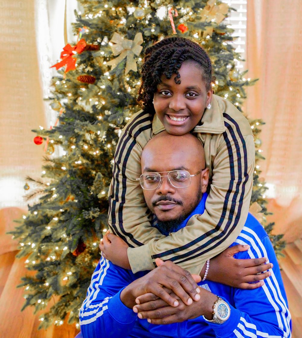 Couple in matching Adidas tracksuits embracing in front of a decorated Christmas tree.