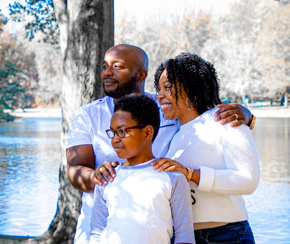 A joyful family wearing white shirts poses together by a lake on a bright day.