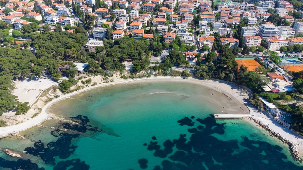 Aerial view of a secluded turquoise bay with sandy beach surrounded by residential buildings in Croatia.