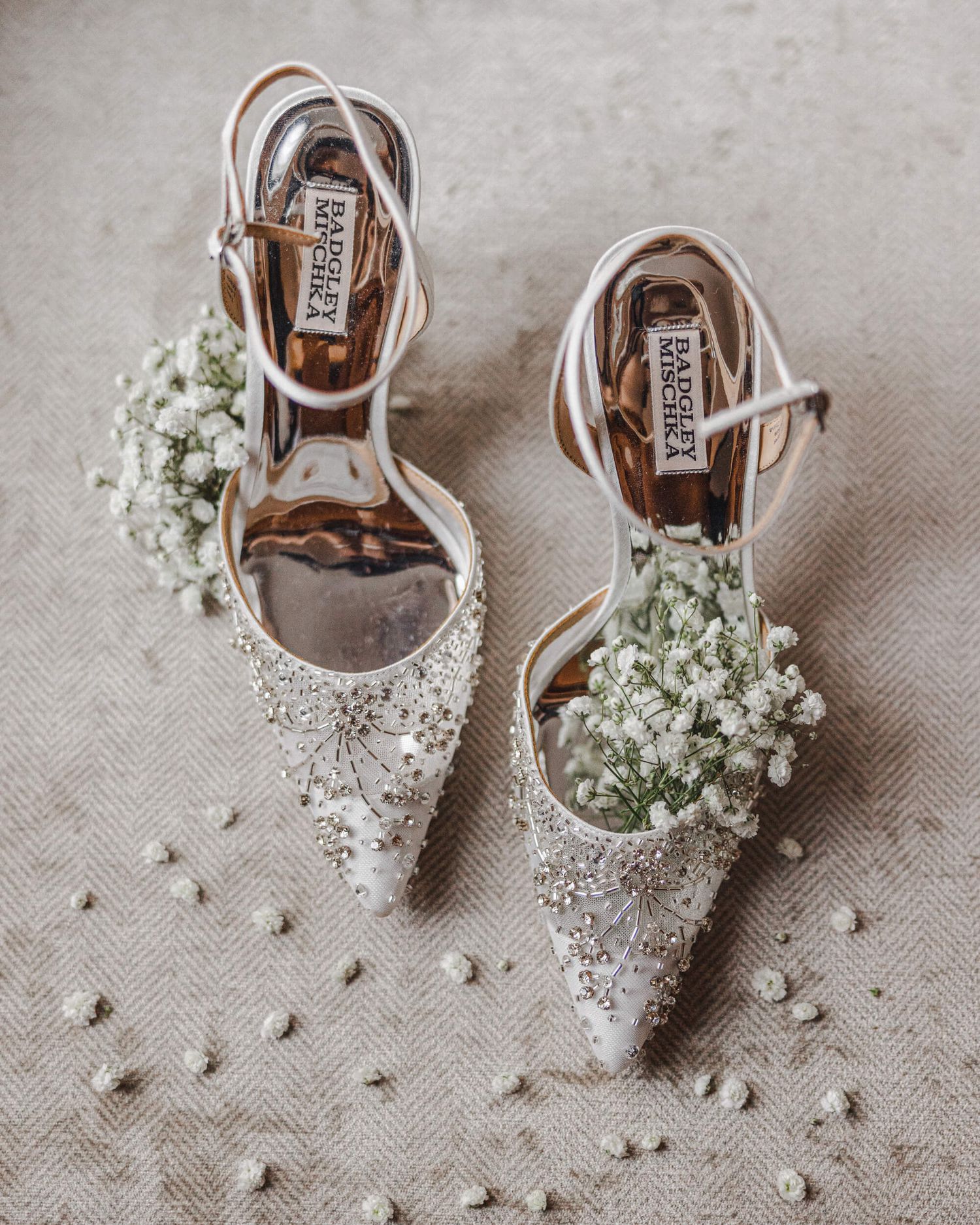 Delicate lace bridal shoes decorated with baby's breath flowers on a light fabric background.