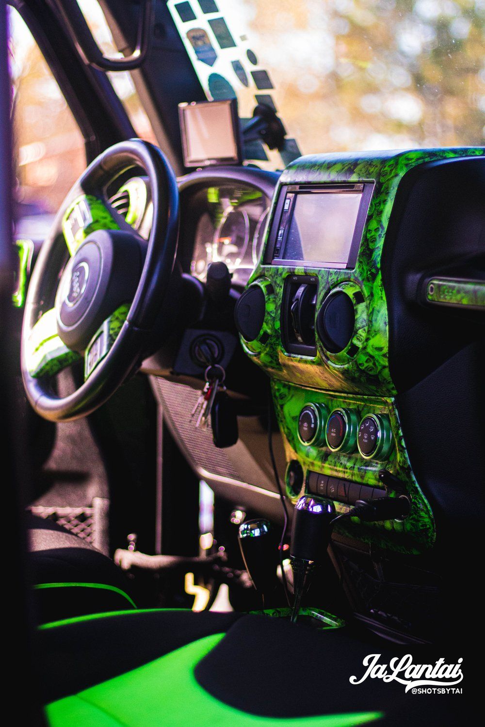 Custom green hydro-dipped interior of a vehicle dashboard with steering wheel and controls glowing in atmospheric lighting.