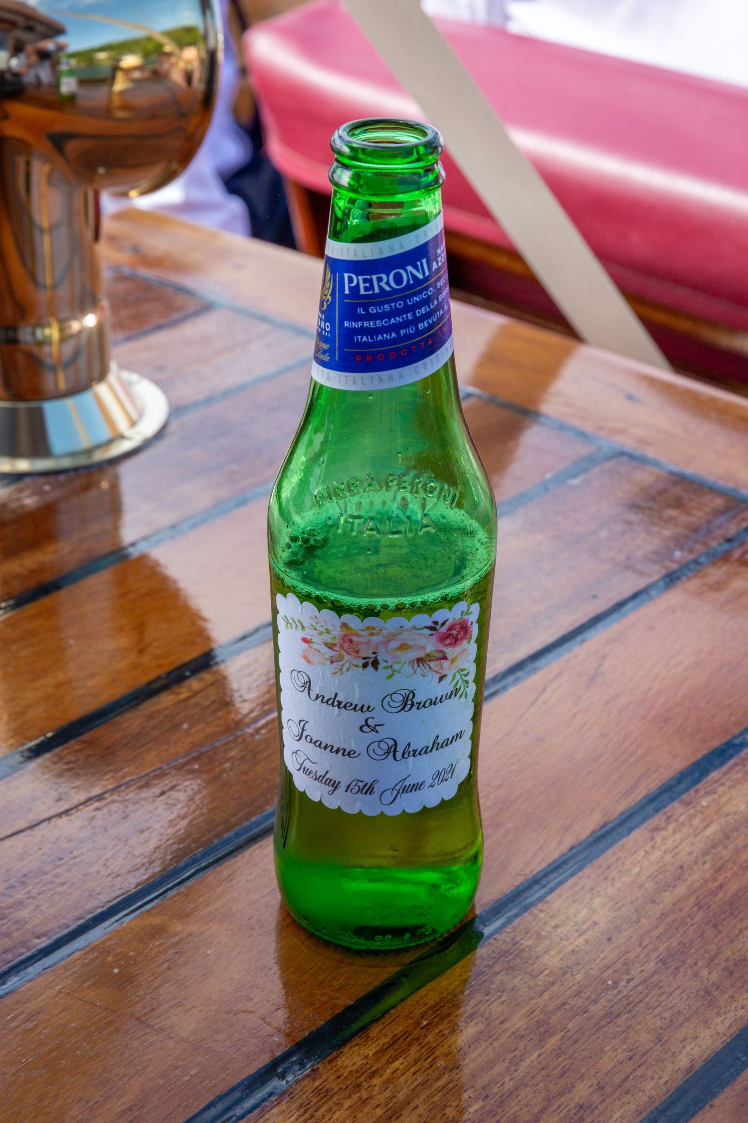 a bottle of peroni lager with a personalised label with the names and wedding date sits on the wooden side of the boat