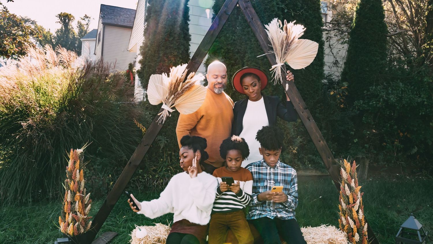 Joyful family of five poses under a rustic wooden triangle arch decorated with dried pampas grass outdoors.
