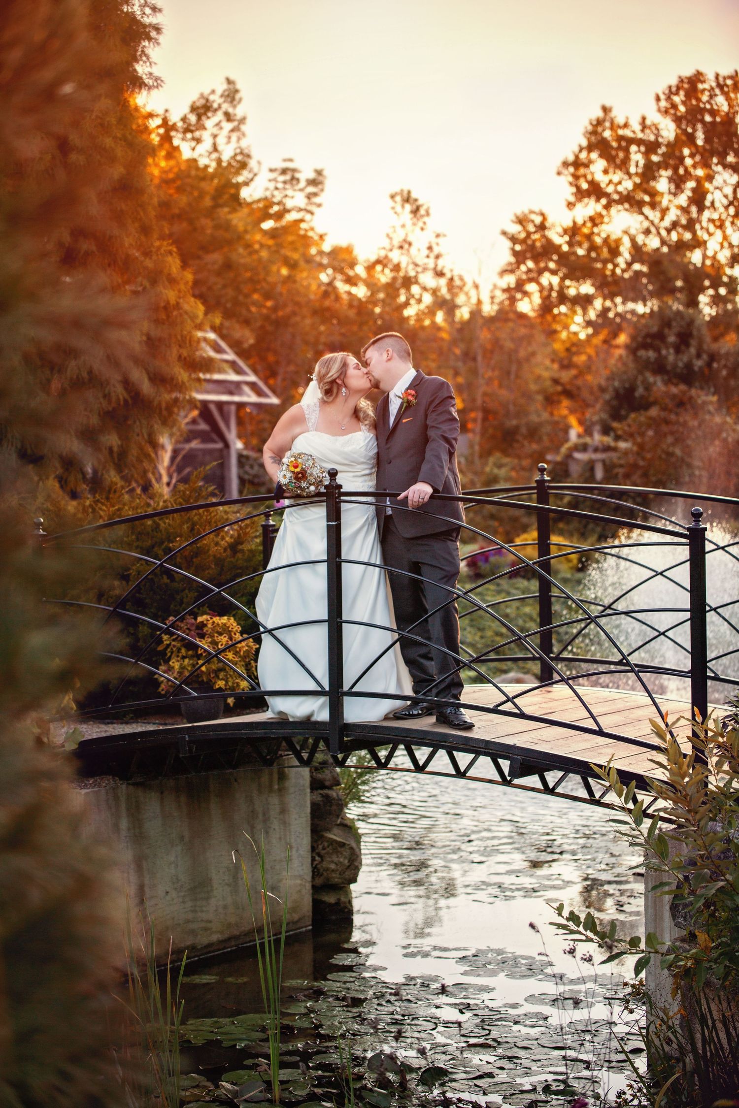 A couple shares a romantic moment on a rustic bridge at sunset with autumn foliage in the background.