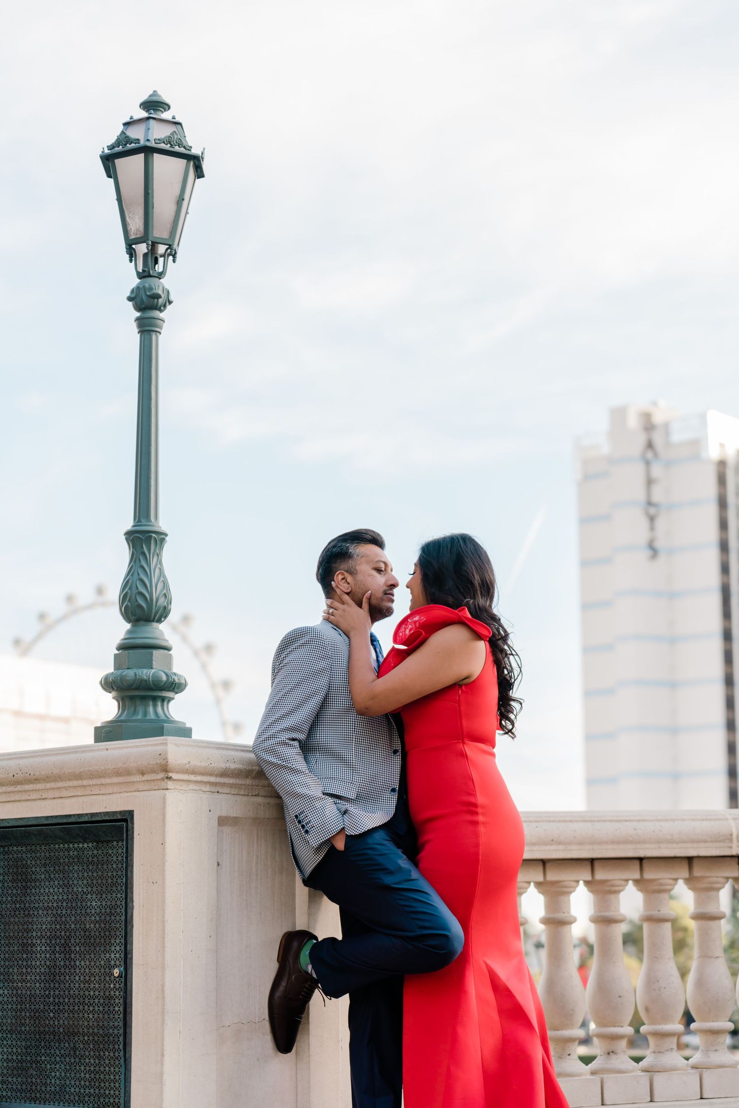 A romantic couple embraces by a vintage lamppost, with the woman wearing a striking red dress.