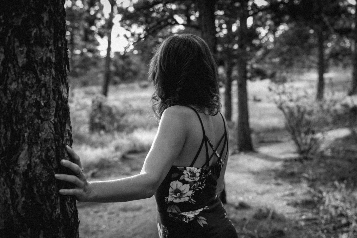 Black and white photo of someone touching tree trunk in forest setting.