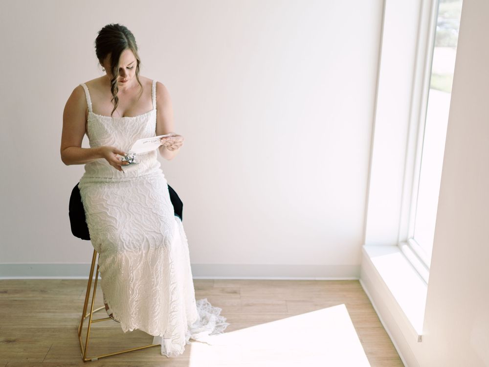 Bride reading Groom's letter sitting indoors at The Eloise bright sun. Classic and film-inspired wedding photography in Madison, Wisconsin.