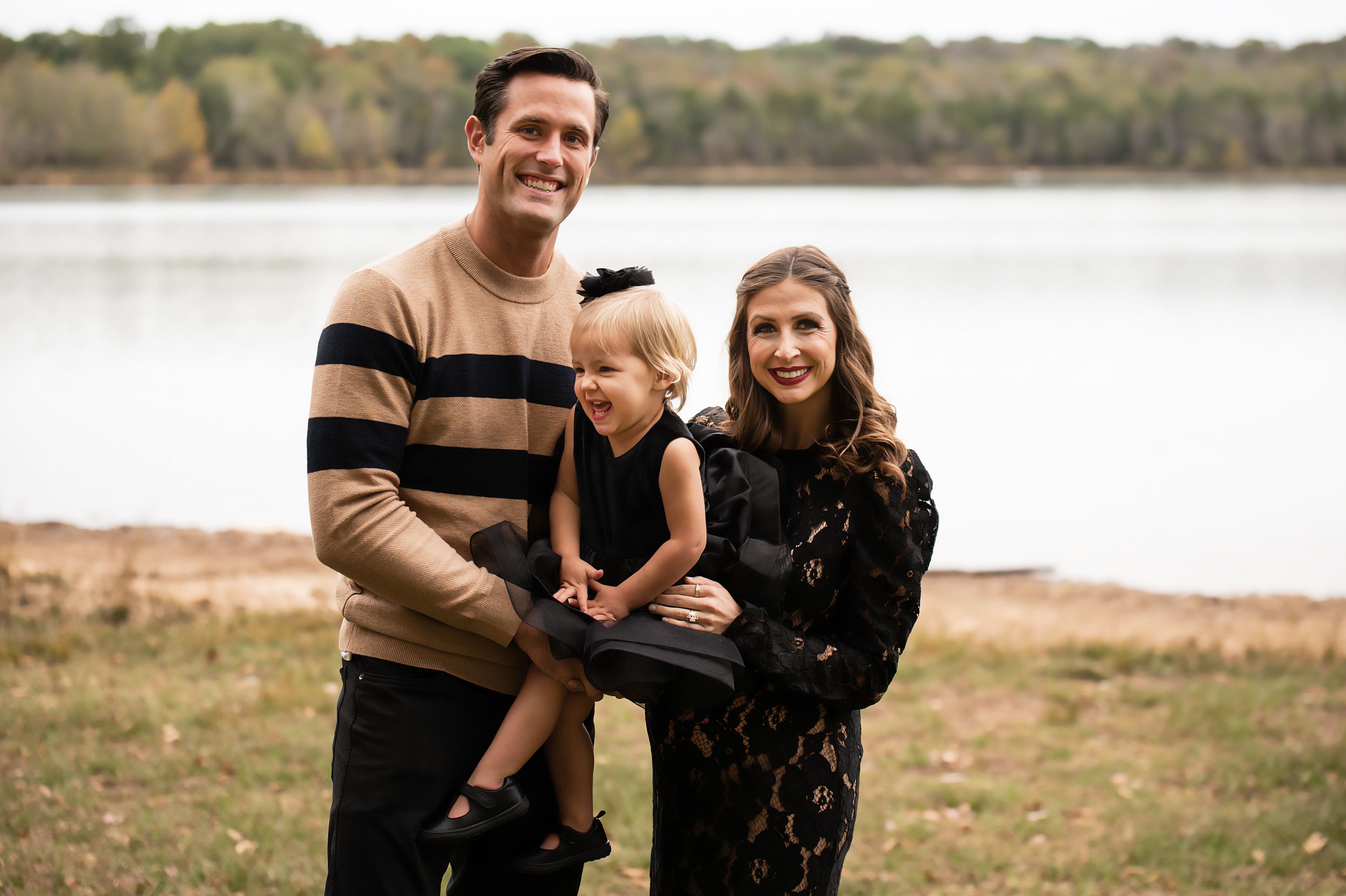 A family poses together on an autumn day by a serene lake.