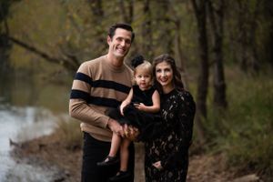 A family portrait taken in a wooded area near water during fall season.