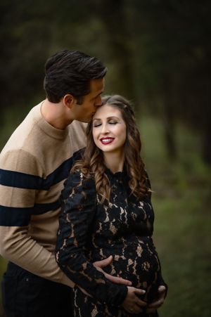 A maternity photo featuring a couple in autumn attire against a forest backdrop.