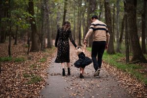 A family walks together on a leaf-covered path through an autumn forest.