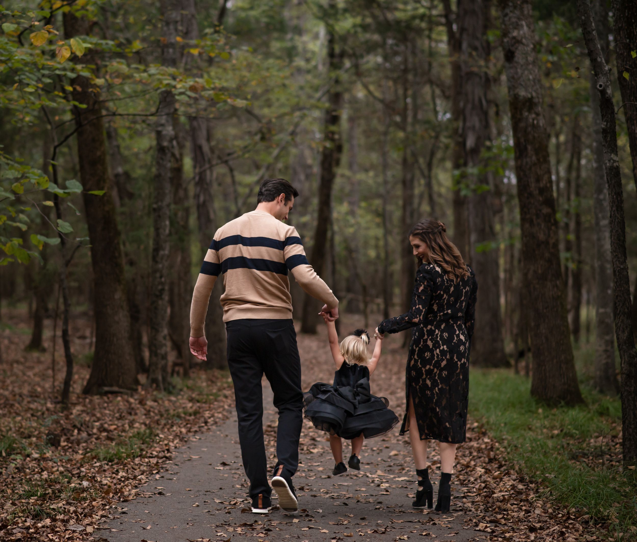 A couple and young child walking together on an autumn path through a wooded forest.