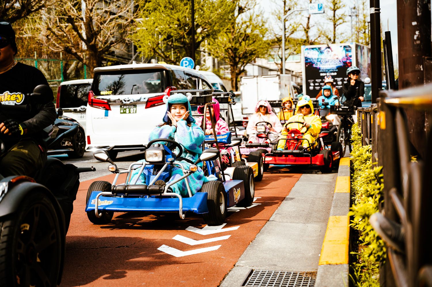 Colorful go-karts racing on a street lined with trees in an urban setting.