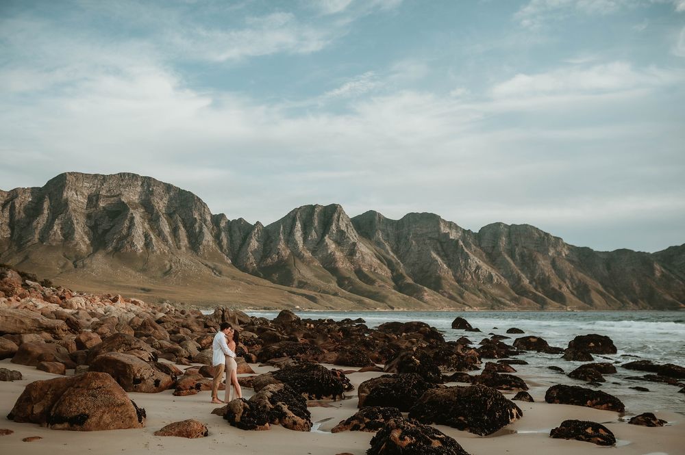 Rocky coastline with dramatic mountain backdrop and black boulders scattered along the beach.