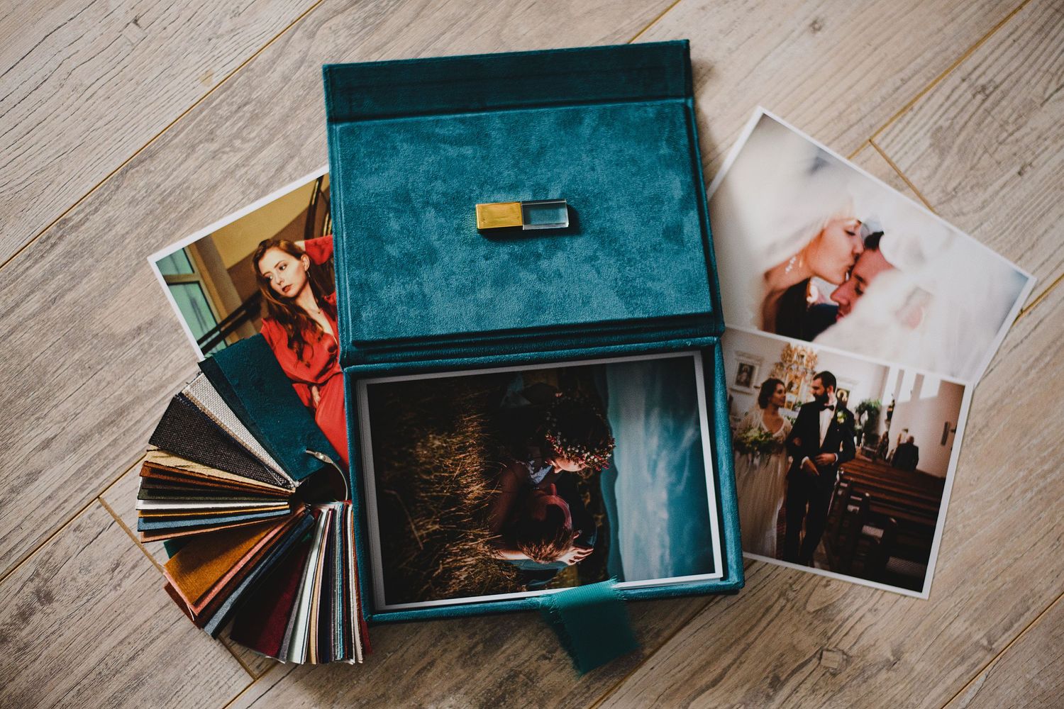A teal velvet photo box with printed photographs scattered around it on a wooden floor.