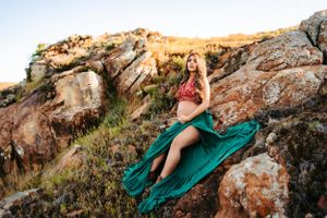 A dramatic maternity photo on rocky cliffs at golden hour with flowing green dress.