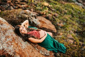 A creative maternity photo on rocky terrain with woman in red top and flowing green skirt.