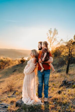 A family of three stands together against a sunset mountain backdrop.