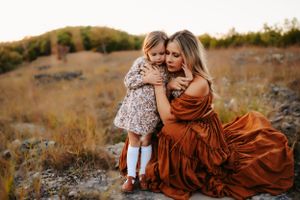Intimate family moment captured against autumn landscape with flowing rust dress.