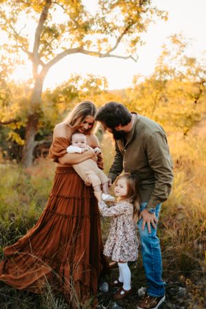 Family embracing outdoors with flowing rust-colored dress against golden fall foliage.
