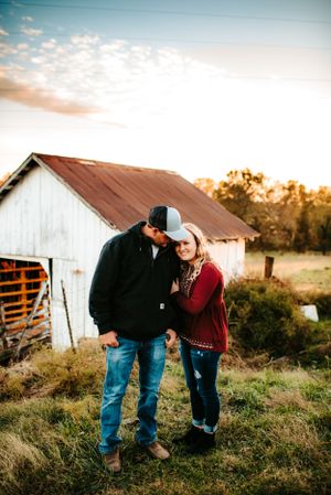 A couple shares an intimate moment together near a rustic white barn at sunset.