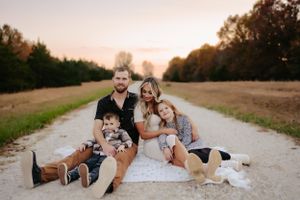 Family relaxing together on a dirt path surrounded by autumn fields.