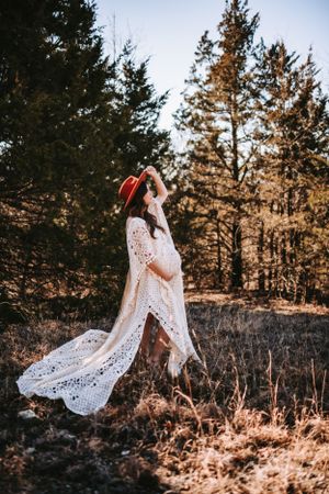 A flowing white lace dress catches the sunlight in a forest maternity photo.