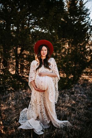 A dreamy maternity photo captures a special moment in a forest setting at sunset.