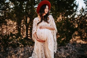 Ethereal maternity photo featuring flowing white lace dress and red hat in golden sunset light.