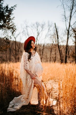 Dreamy maternity portrait in white lace dress among autumn grasses at sunset.