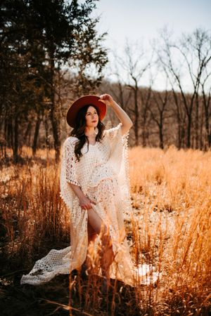 Artistic maternity photo with flowing lace dress and red hat in golden field.