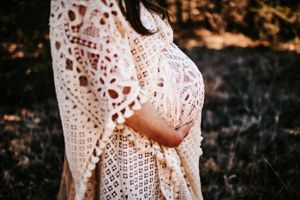Close up view of a delicate white lace dress worn by an expectant mother.