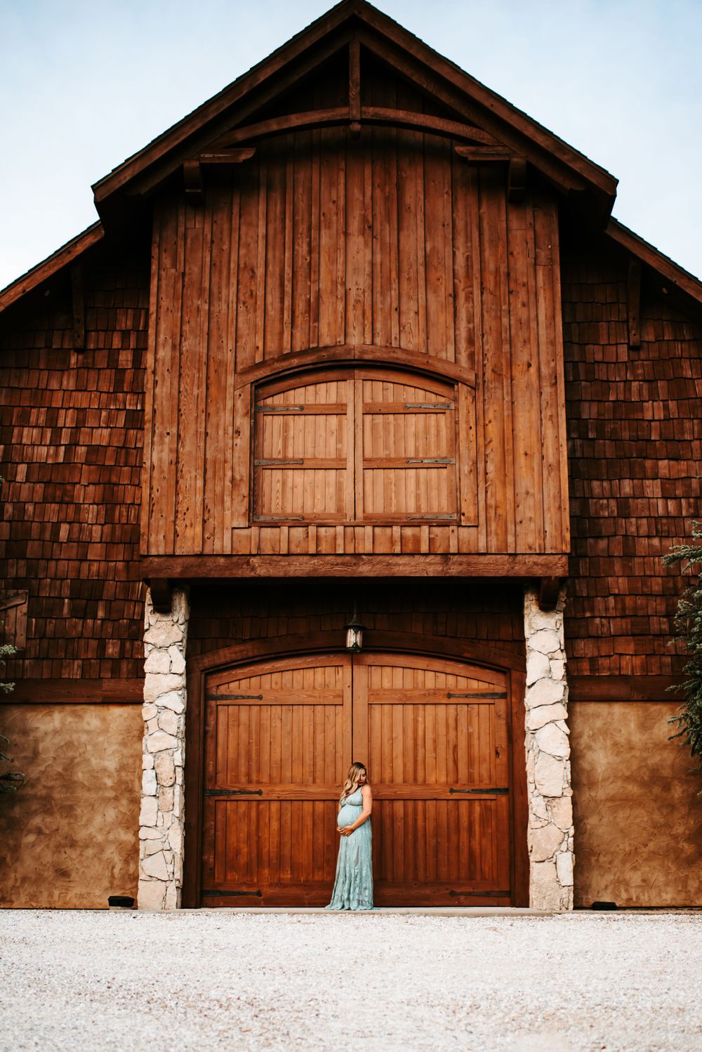 Rustic wooden barn with large doors and stone pillars against warm lighting.
