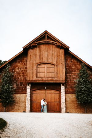 Large wooden barn with cedar shingles and double doors on gravel path.