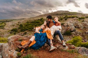 A candid family moment captured on a rocky hillside with stormy clouds in background.