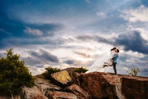 A silhouette of a couple embracing on rocky outcrop against dramatic cloudy sky.