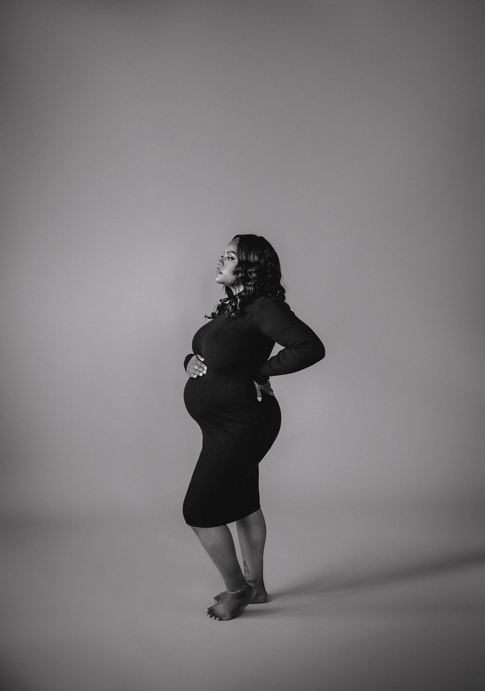 Silhouette of pregnant woman in black dress against grey background.
