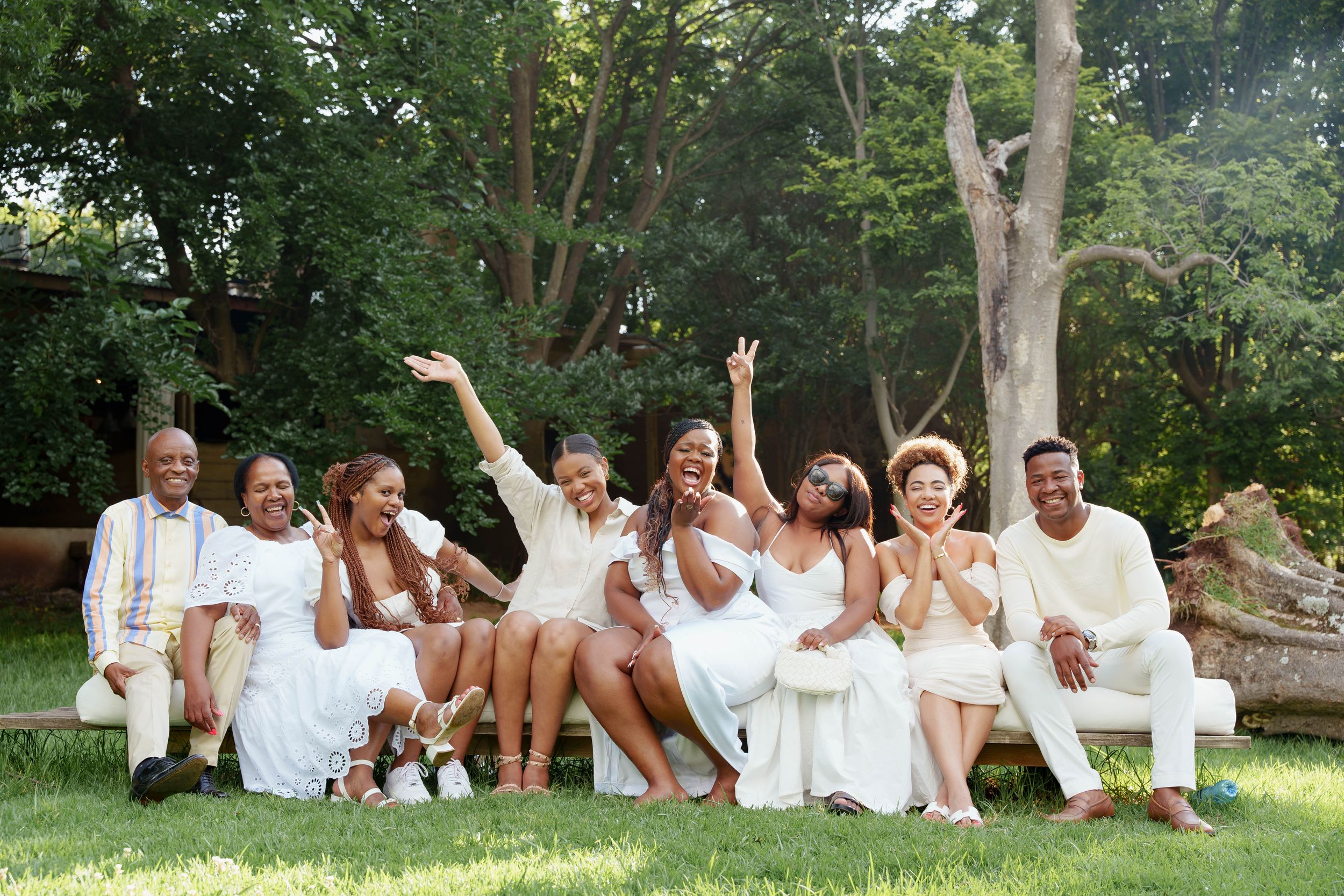 A celebratory group poses on grass in coordinated white outfits.