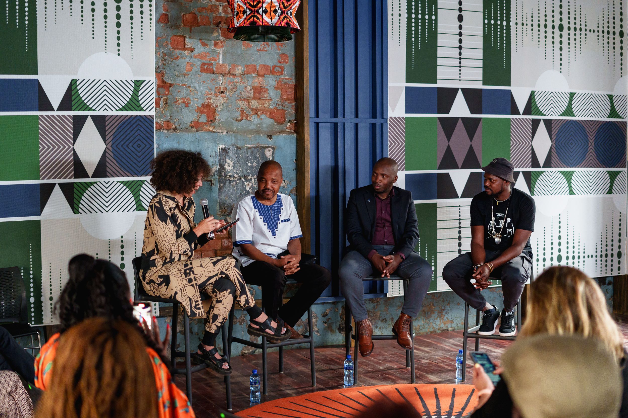 A panel discussion event with audience members in a room decorated with geometric patterns.