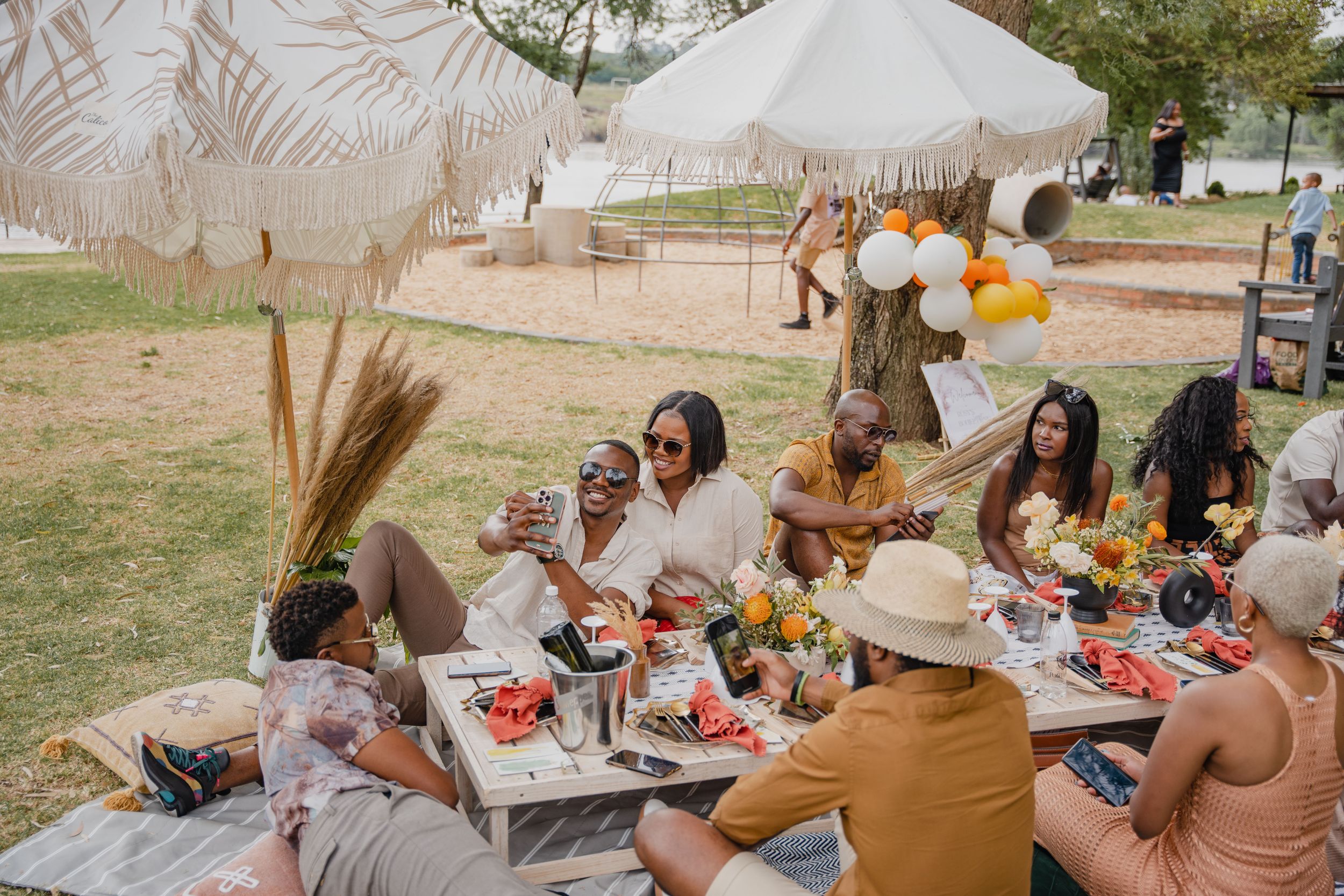A casual outdoor gathering with friends enjoying food and drinks under umbrellas.