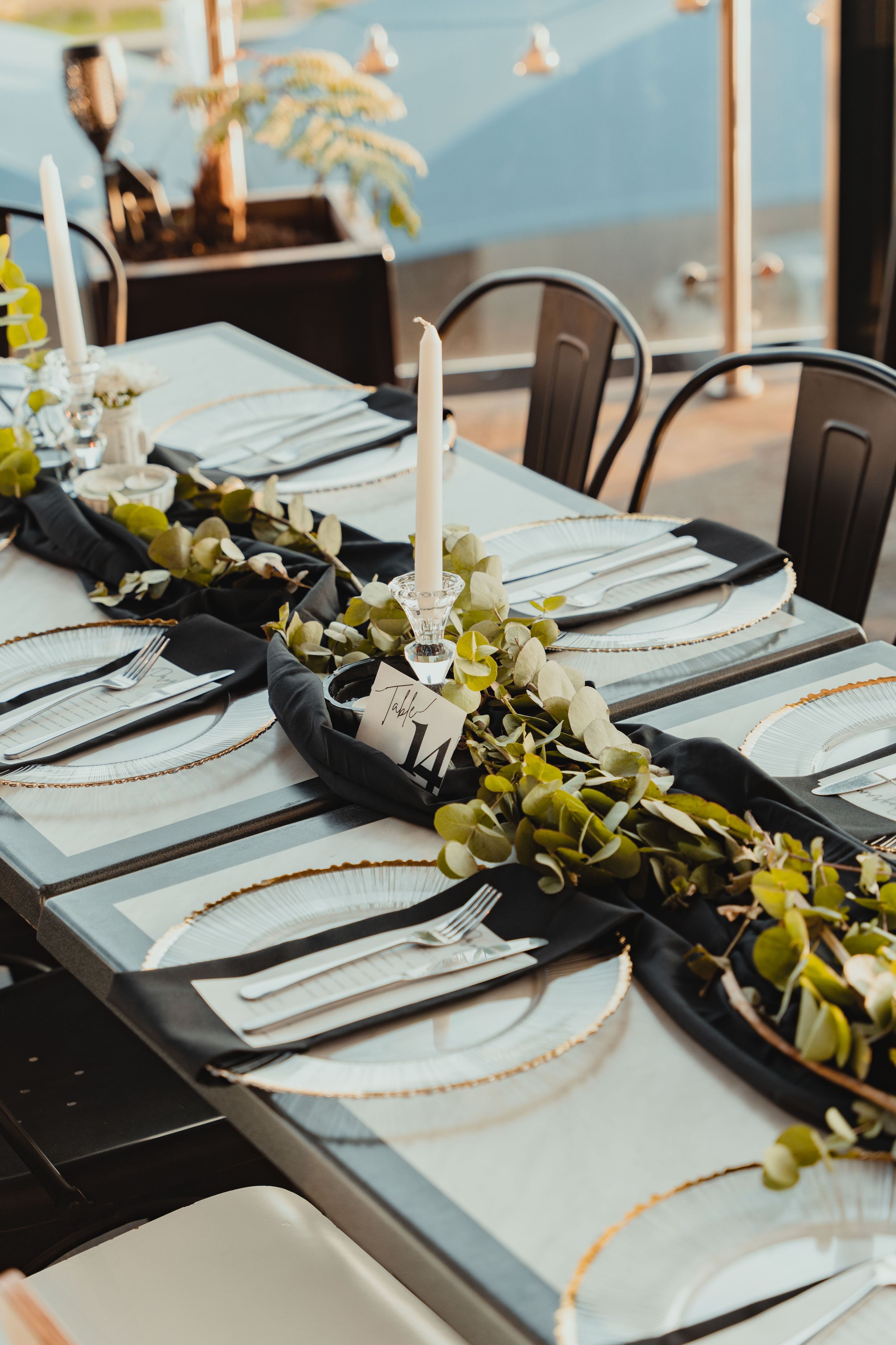 Elegant table setting with white plates, black napkins and eucalyptus garland runner.