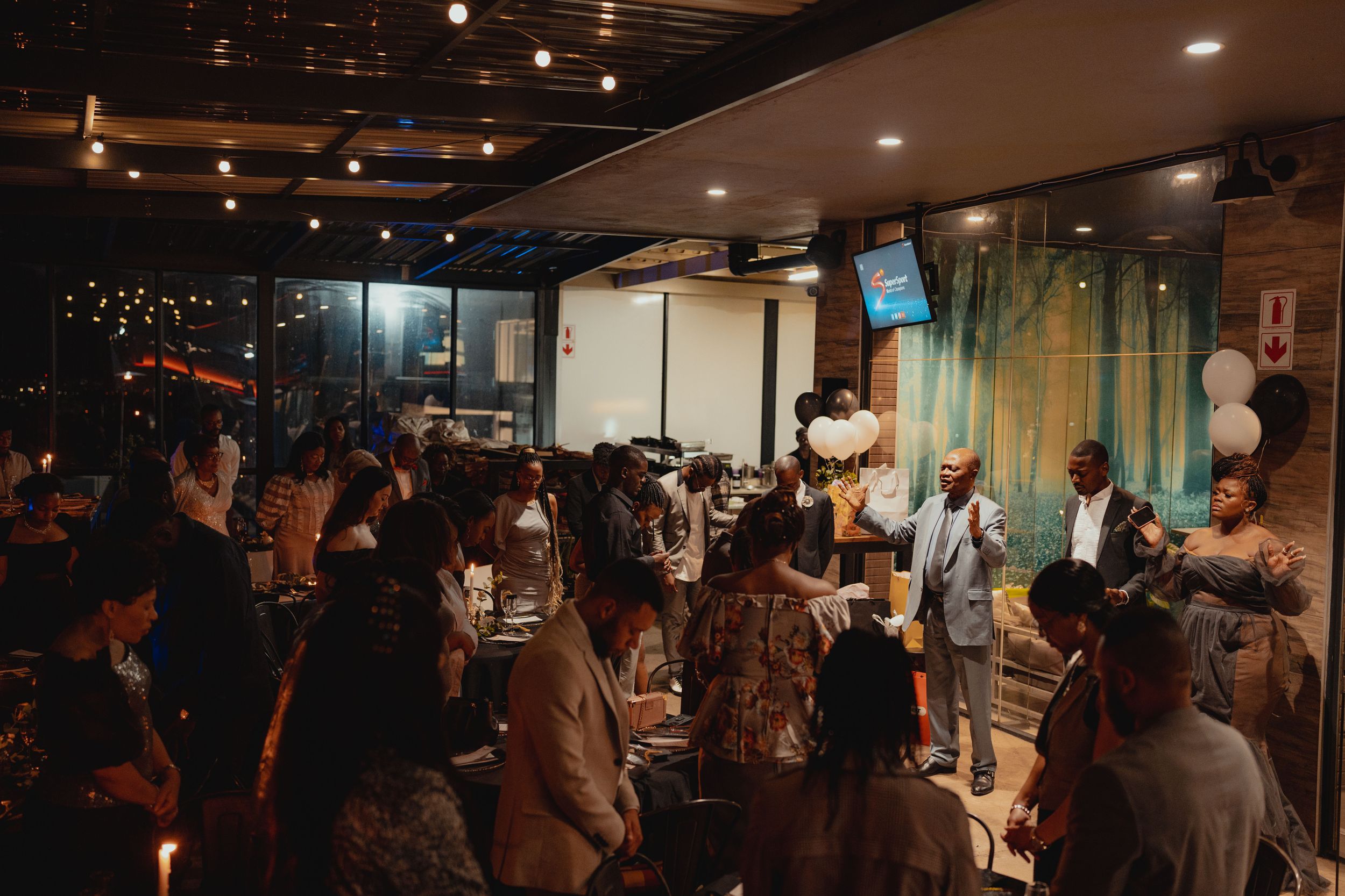 Crowded indoor event space with string lights and people mingling.
