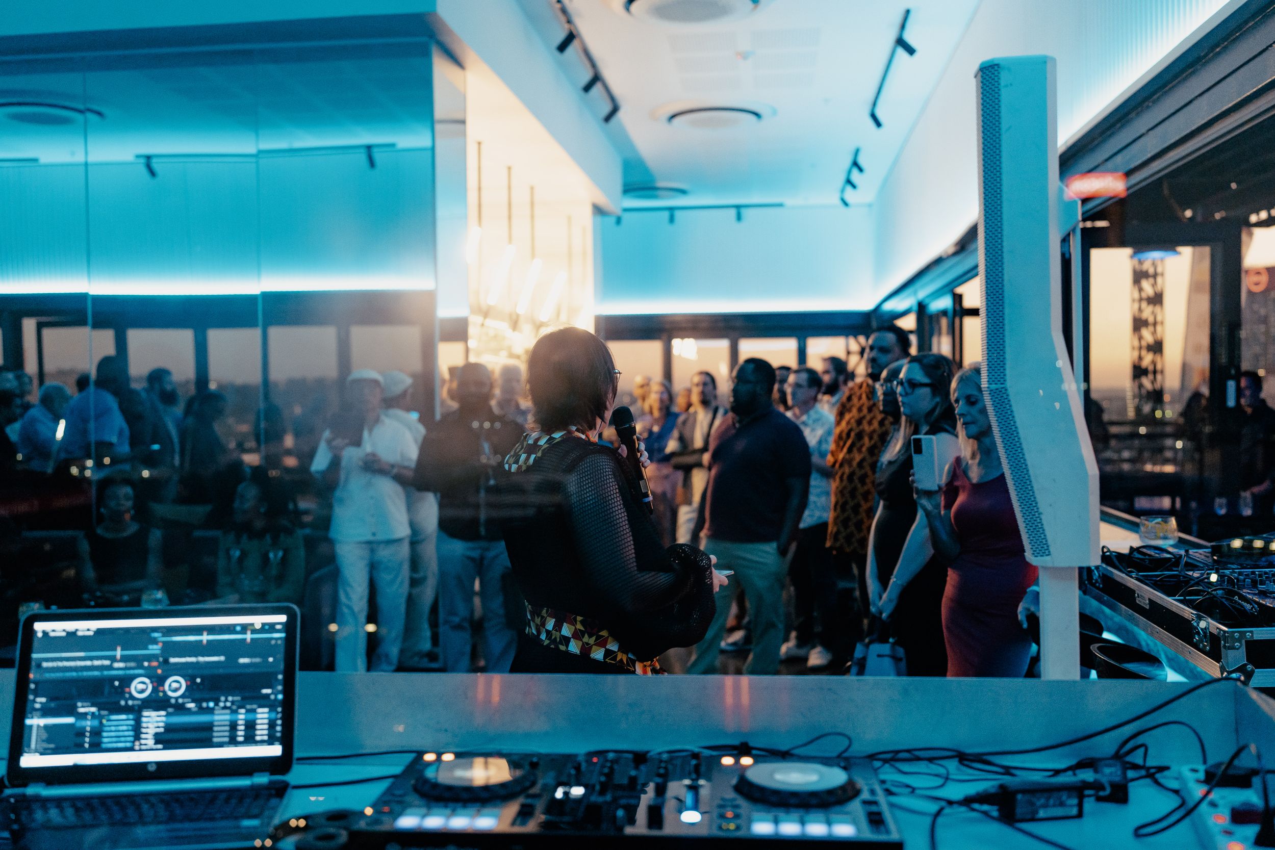 DJ equipment setup in a modern venue with blue lighting and crowd in background.