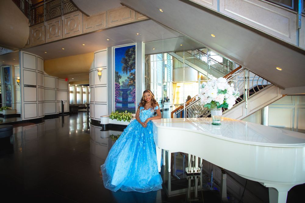 Cinderella-style photoshoot in blue ballgown near grand white piano in luxurious venue.