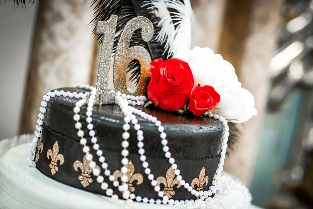 Elegant black wedding cake with pearl strands and red rose accents.