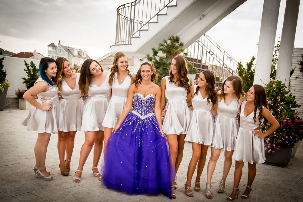 A group in white dresses poses together with one person wearing a stunning purple ballgown in the center.