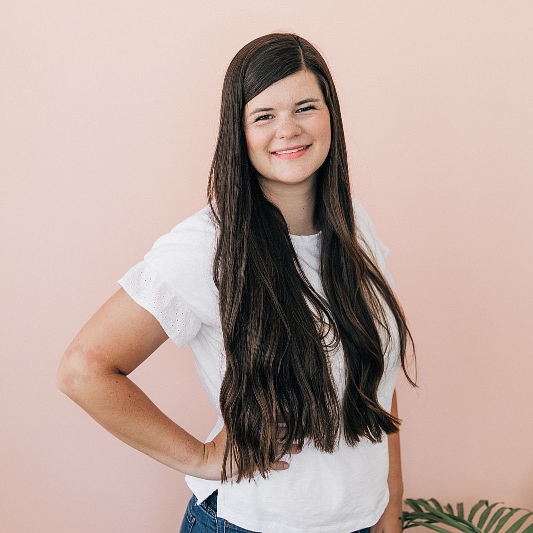 Studio portrait against pink backdrop featuring casual white t-shirt and long dark hair.