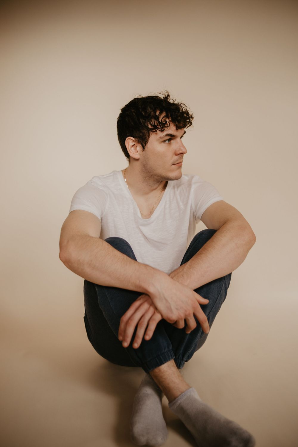 Artistic portrait with person sitting cross-legged against warm beige background.