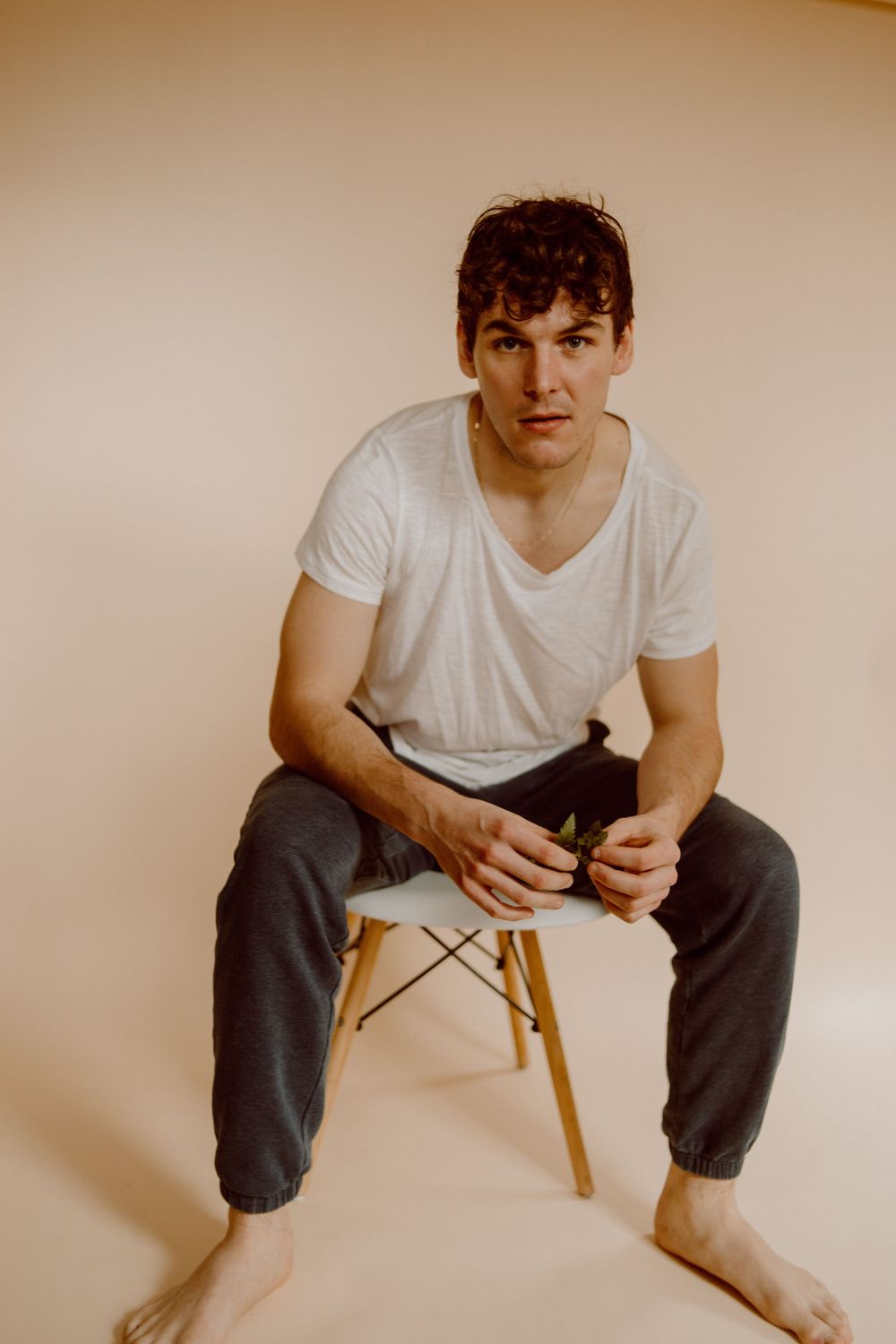 Casual portrait of person seated on wooden stool wearing white t-shirt and dark pants.